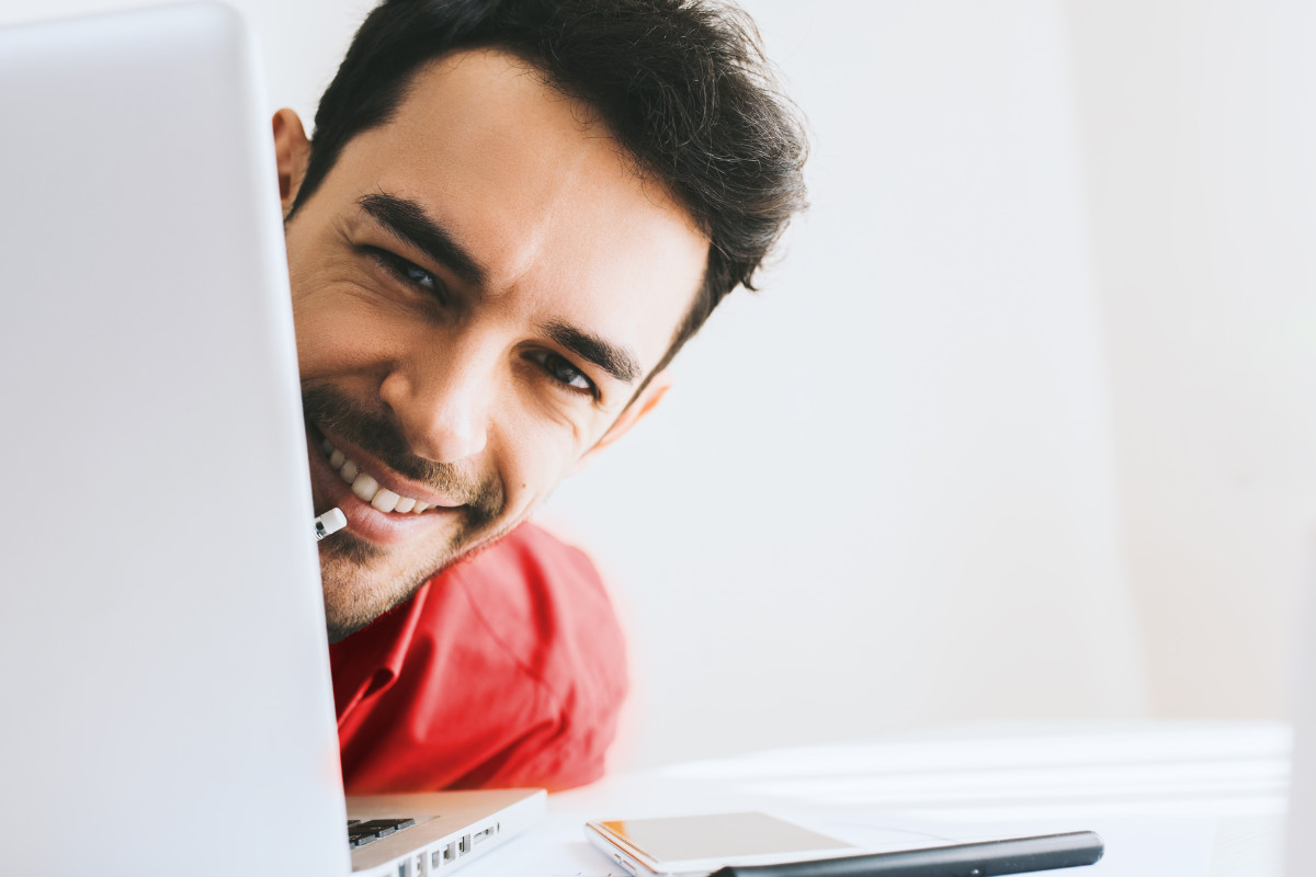 Man smiling behind a laptop screen